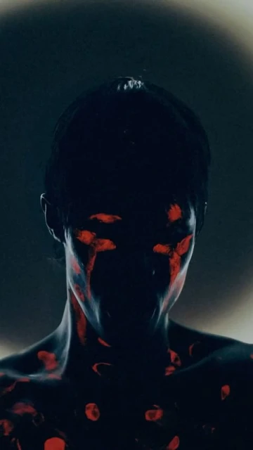 Dramatic portrait of a person with dark skin and red body paint. Artistic face and body painting in a dark environment.