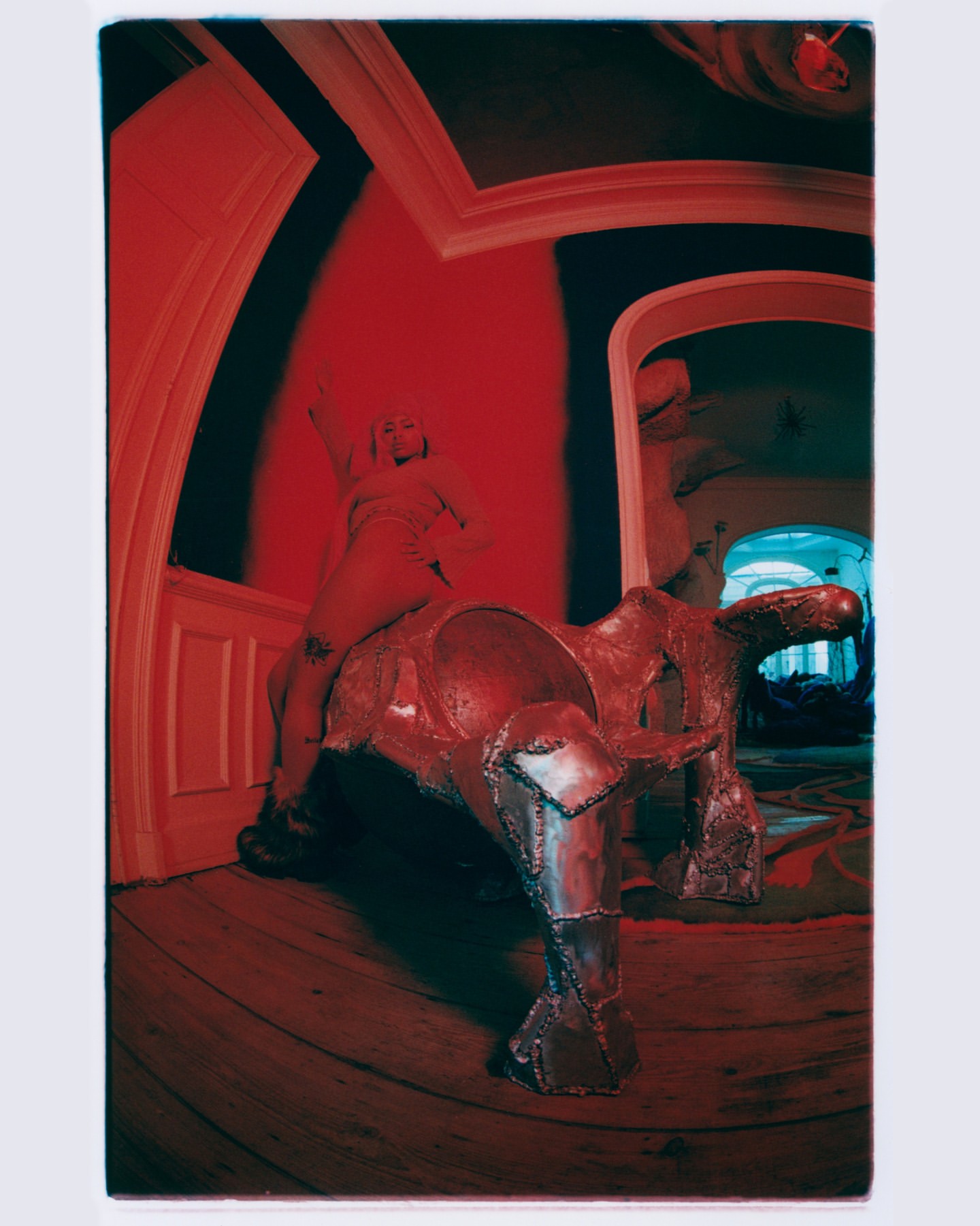 Photo of a woman on top of a sculpture resembling a horse inside a room with a red color cast and a wide angle lens.