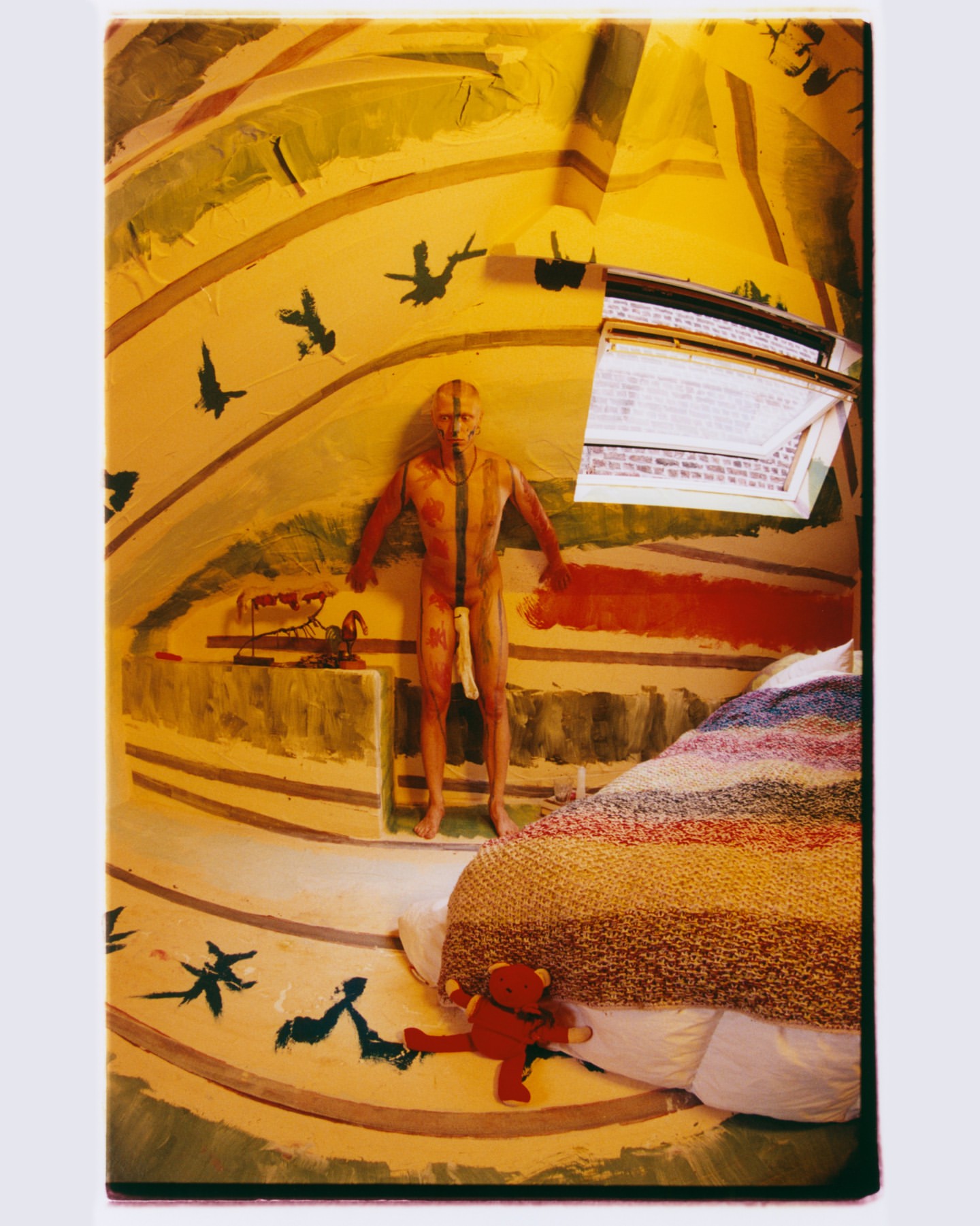 Artistic bedroom interior features a painted male figure, striped bedding, and teddy bear, creating a surreal and creative space.