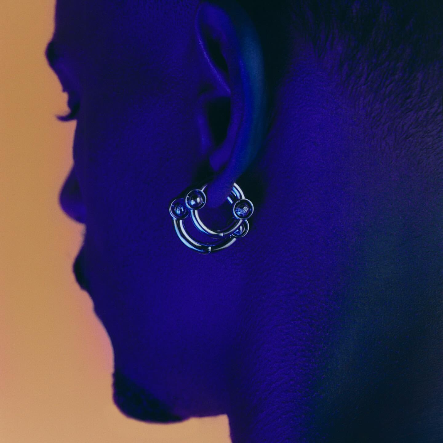 Close-up studio shot of a silver hoop earring with small spheres on an adult human's ear, illuminated with blue lighting.