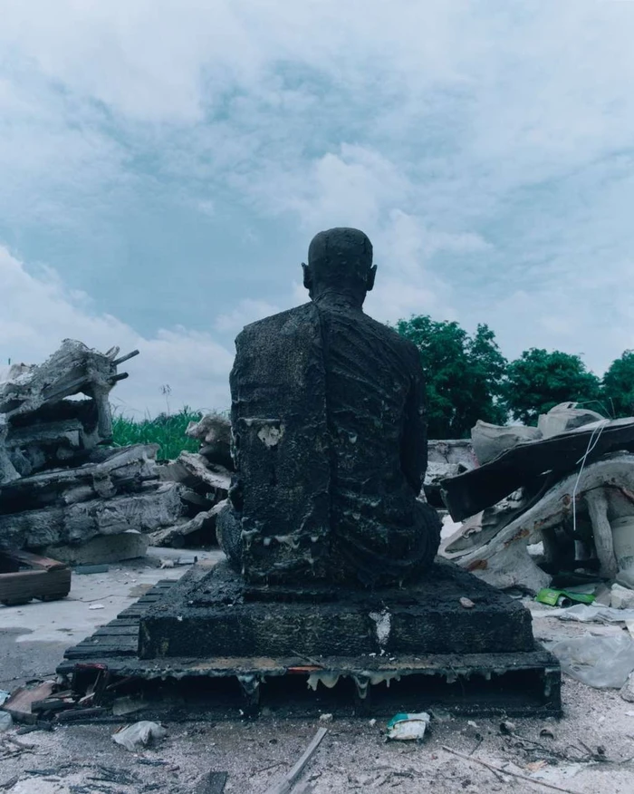 Rear view of a dark textured statue seated amidst concrete rubble under an overcast sky, photographed by Lee Wei Swee.