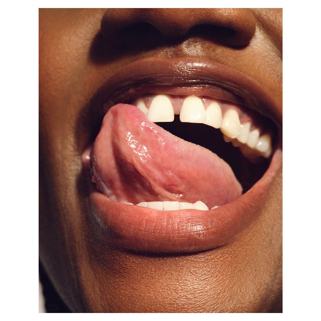 Close-up of an adult female with brown skin and white teeth sticking out her tongue in an indoor studio environment.