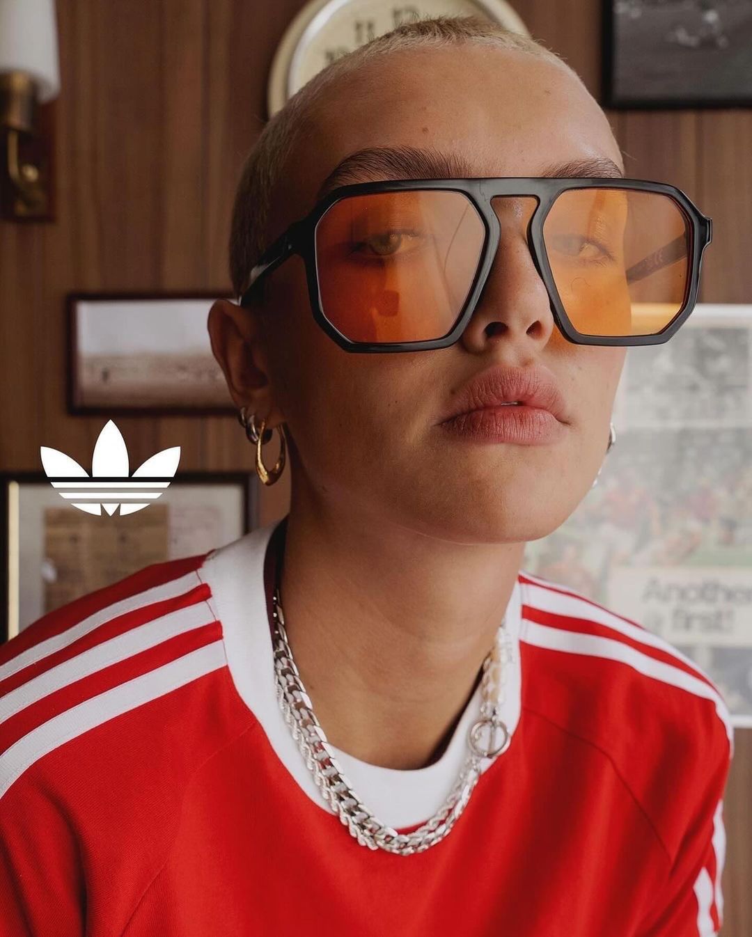 Close-up of a short-haired person with a red and white Adidas shirt and glasses in an indoor setting with a wooden background.