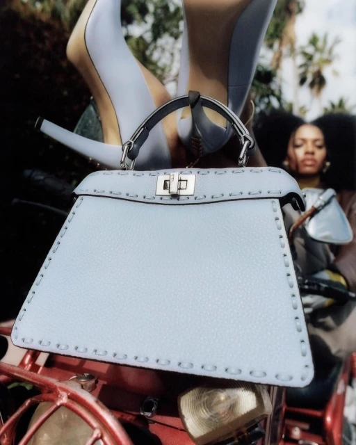 Light blue leather handbag with silver hardware, high heels, and an adult woman against a background with palm trees.