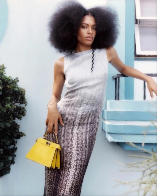 Elegant African-American woman in dress poses outdoors near steps with a yellow handbag, displaying fashion and style.