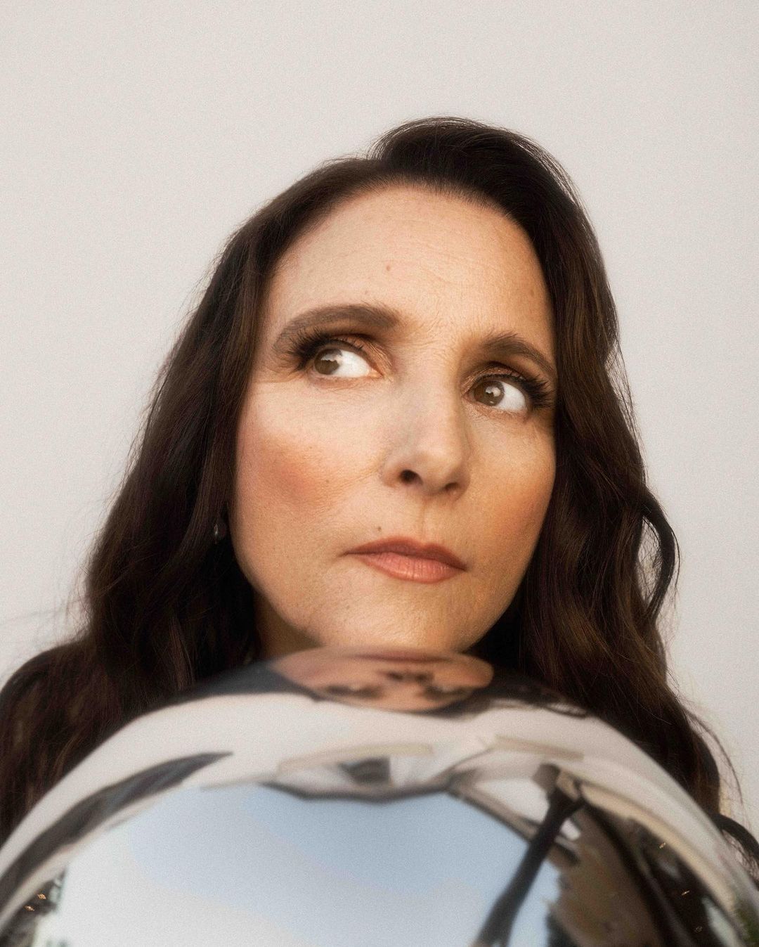 Portrait of a woman looking to the side with a reflective silver sphere in the foreground, set against a neutral background.