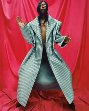 Model in wide-collared striped coat wearing light eyeshadow against a draped red fabric backdrop