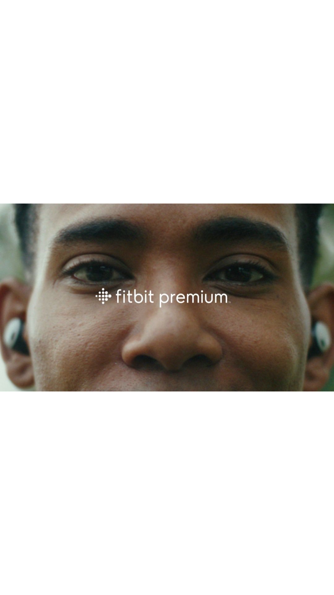 Close-up of a person wearing wireless earbuds with the FitBit Premium logo on the image, suggesting a focus on fitness and technology.