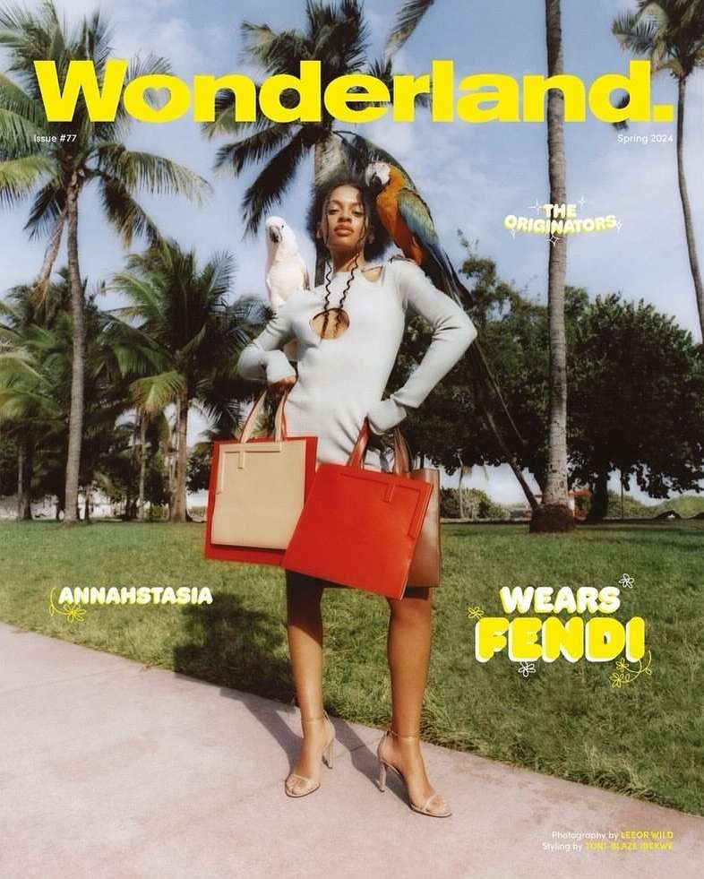 Wonderland Magazine cover featuring a woman in a grey dress with colorful parrots, holding red and tan tote bags in an outdoor setting.