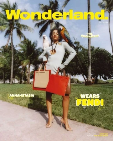 Wonderland Magazine cover featuring a woman in a grey dress with colorful parrots, holding red and tan tote bags in an outdoor setting.