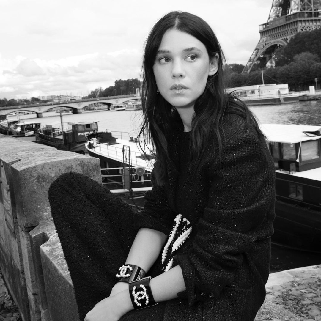 Black and white portrait of a woman with dark hair sitting on a wall with the Eiffel Tower in the background in Paris, France.