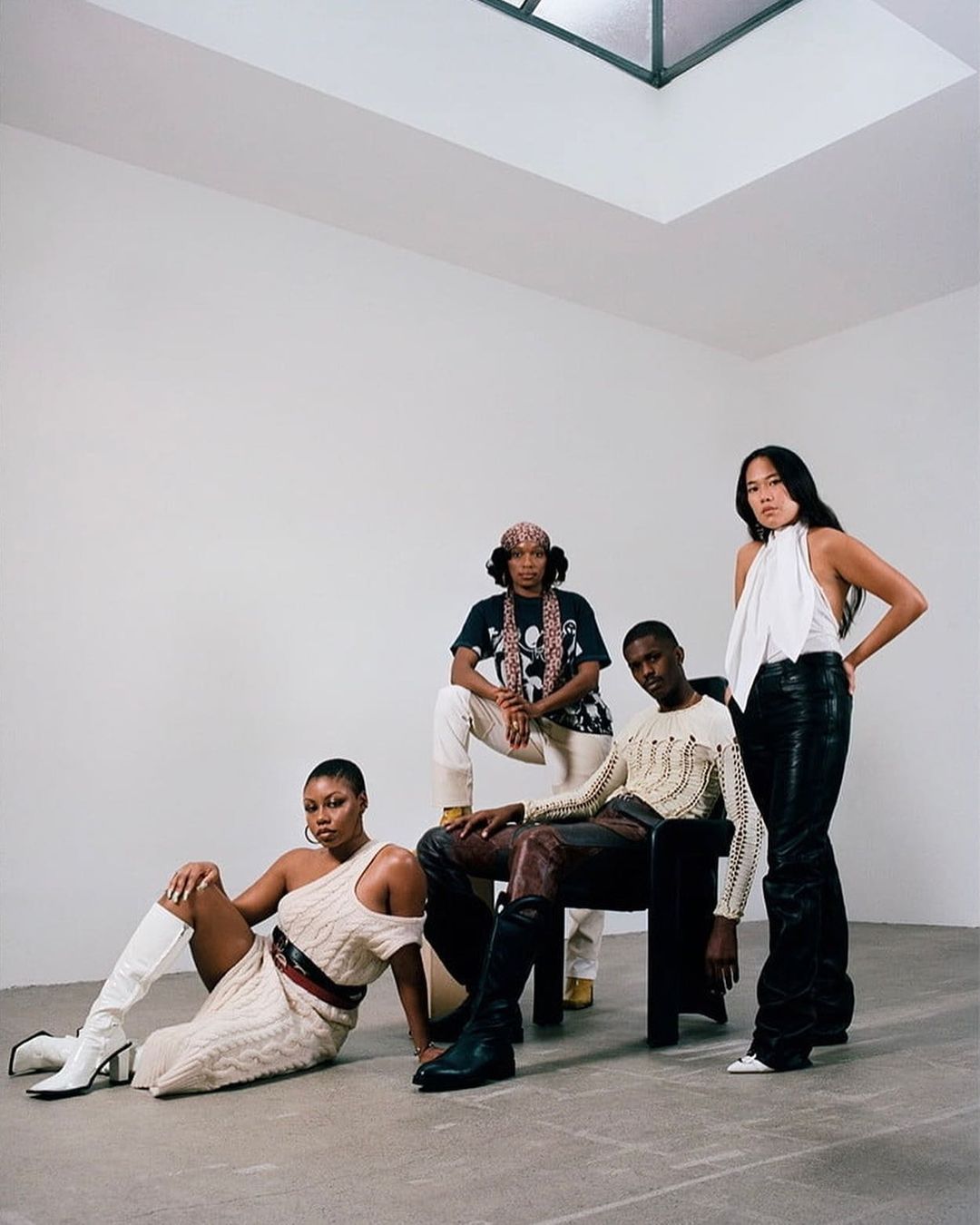 A group of four fashionably dressed adult models pose in a bright white studio with a skylight, showcasing diverse styles and textures.