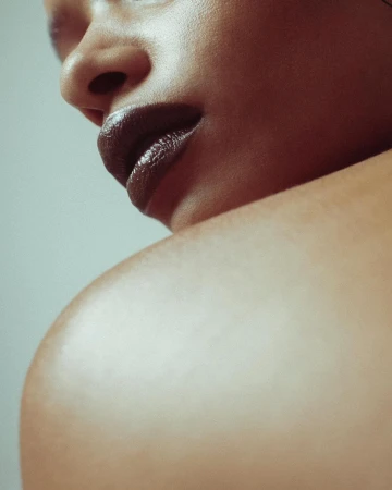 Close-up beauty portrait of a person with dark glossy lipstick and bare shoulder photographed by Lelanie Foster