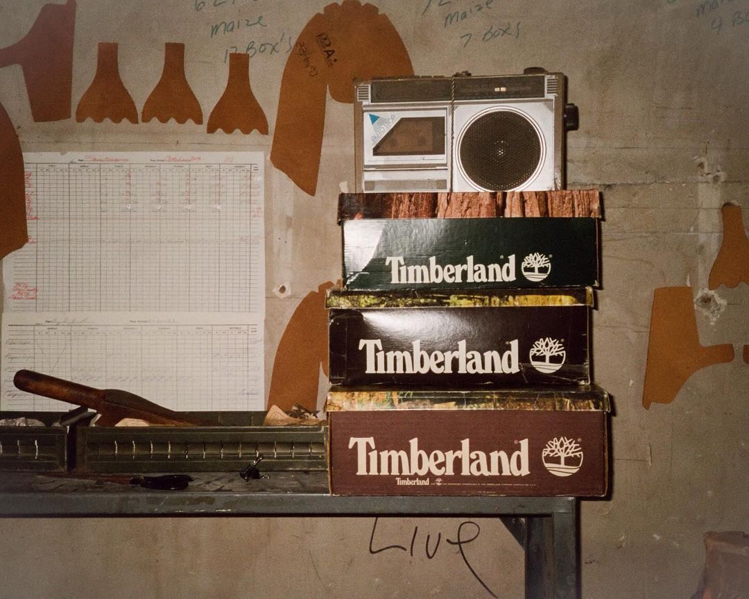 Stack of Timberland shoeboxes topped with a boombox on a metal table against a concrete wall adorned with hand-drawn notes and diagrams.