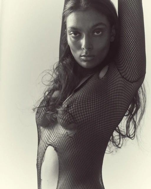 Striking black-and-white portrait of an adult female model in a torn fishnet top, posed against a plain white background.