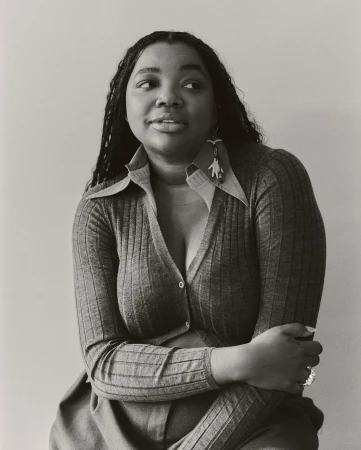 Black and white portrait of an African American woman wearing a cardigan and earrings, looking to the side with a neutral expression.