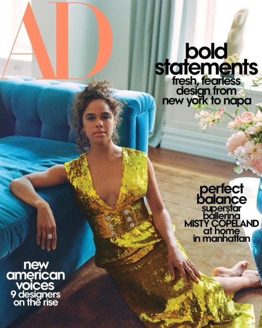 Misty Copeland poses in a gold sequin dress for Architectural Digest cover, seated on a floor near a blue couch and flowers.