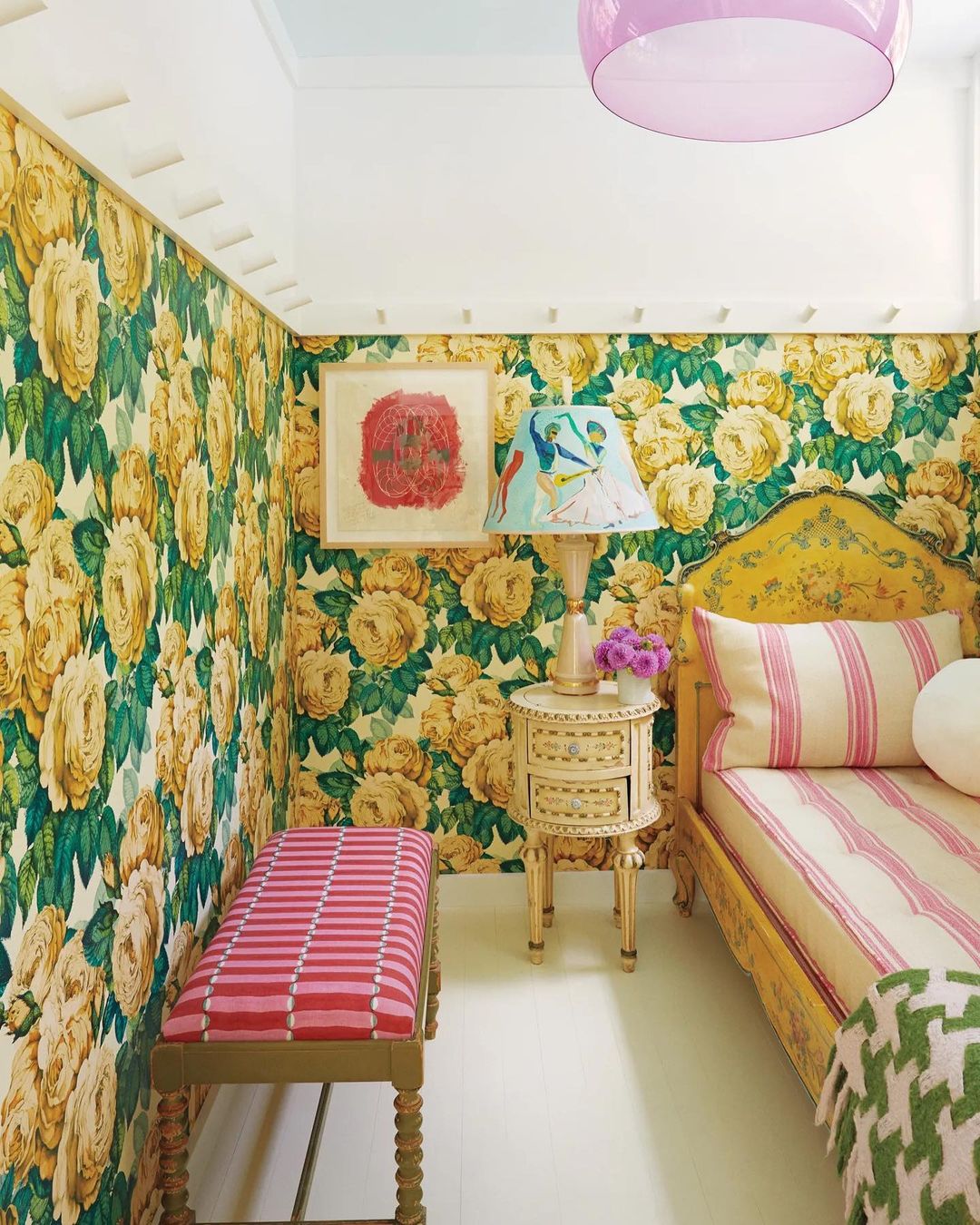 Bedroom interior featuring floral wallpaper, a bed with striped bedding, bedside table with a lamp, and a striped bench.