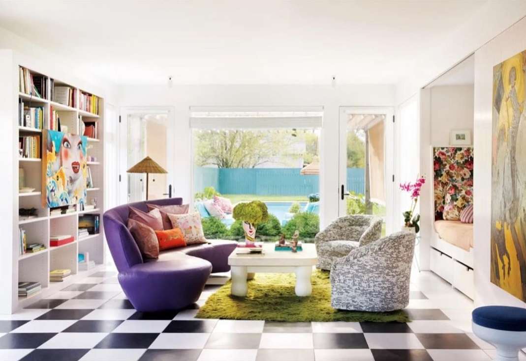 Living room interior with a purple curved sofa, armchairs, and black and white checkered floor tiles, viewed through a wide angle.