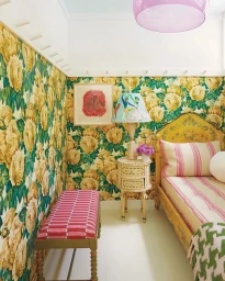Interior view of a cozy bedroom featuring yellow floral wallpaper, a patterned single bed, and pink striped bench.