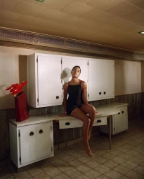 Woman in a black slip dress seated on a white kitchen counter photographed by Lelanie Foster