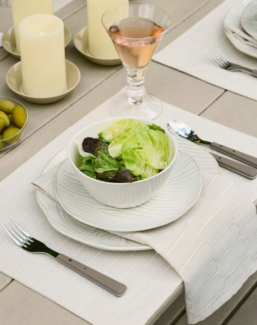 Overhead view of a place setting on a wooden table, featuring a green salad, elegant plates, silverware, candles, and a pink drink.
