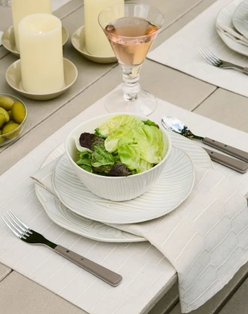 Overhead view of a place setting on a wooden table, featuring a green salad, elegant plates, silverware, candles, and a pink drink.