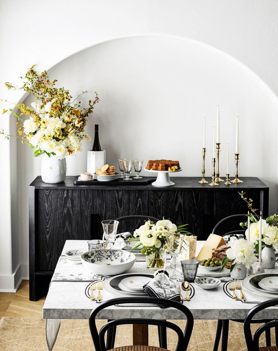 Elegant dining room setup with a dark wood sideboard, flower arrangements, place settings with black chairs, candles, and decorative items.