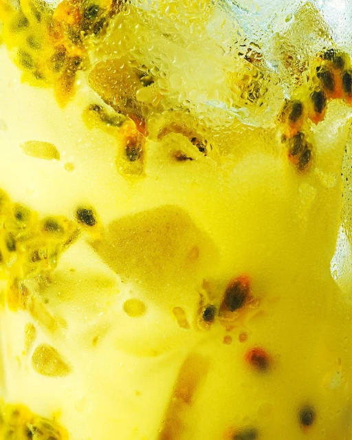 Close-up shot of a refreshing drink with yellow liquid, cubes, and passion fruit seeds, showcasing a chilled beverage for summer.