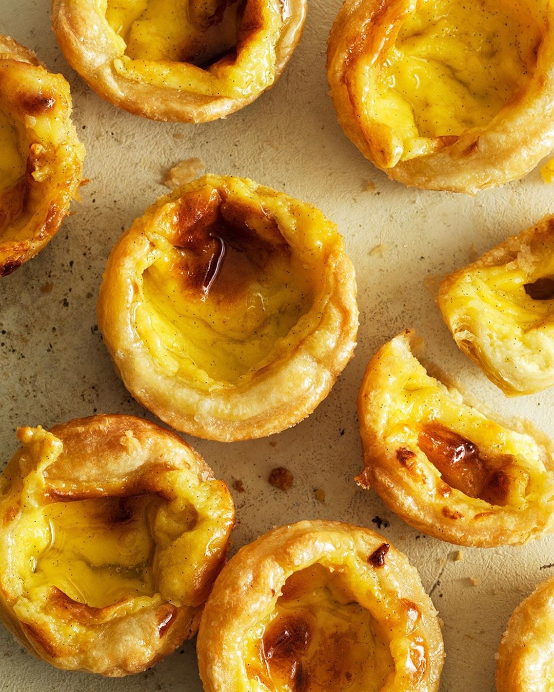 Close-up of a tray of golden-brown Portuguese custard tarts with flaky pastry and a caramelized custard filling.