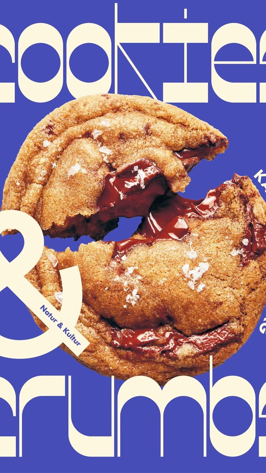 Close-up studio shot of a chocolate chip cookie, part broken, with salt flakes on a blue background with Cookies & Crumbs text.