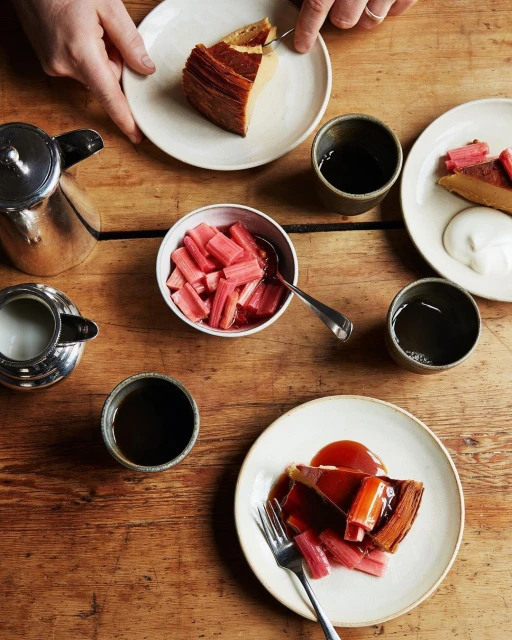 Overhead shot features a table with rhubarb dessert, coffee, and silverware. Rustic, warm tones create an inviting culinary scene.