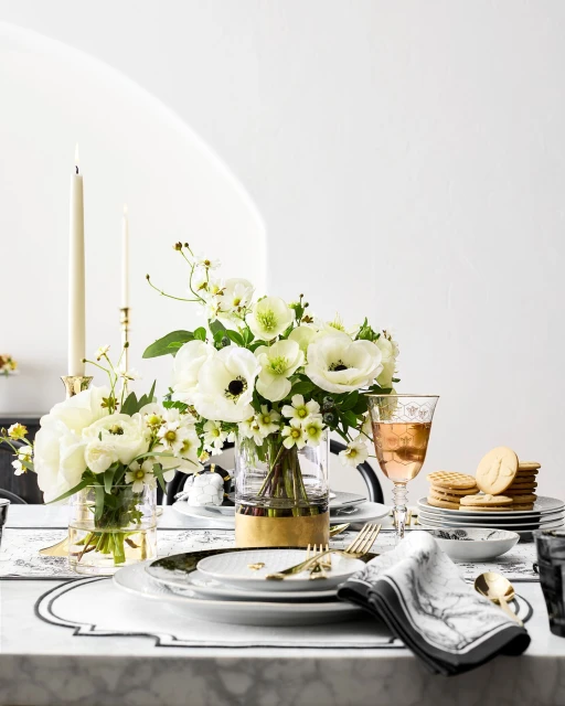Elegant table setting featuring floral bouquets in clear vases, candles in gold holders, layered plates, and decorative napkins.