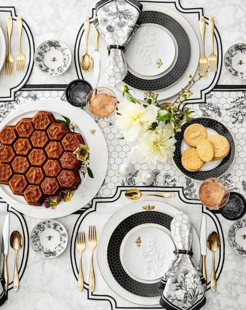 Overhead shot of a table setting with honeycomb cake, floral china plates with bee accents, gold flatware, and white floral centerpiece.