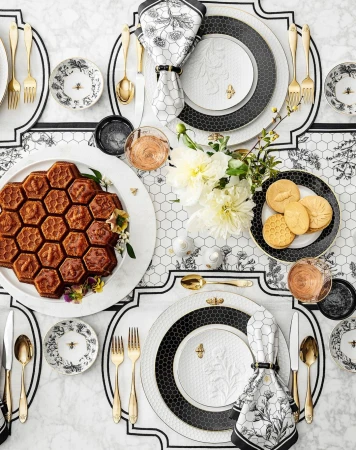 Overhead shot of a table setting with honeycomb cake, floral china plates with bee accents, gold flatware, and white floral centerpiece.