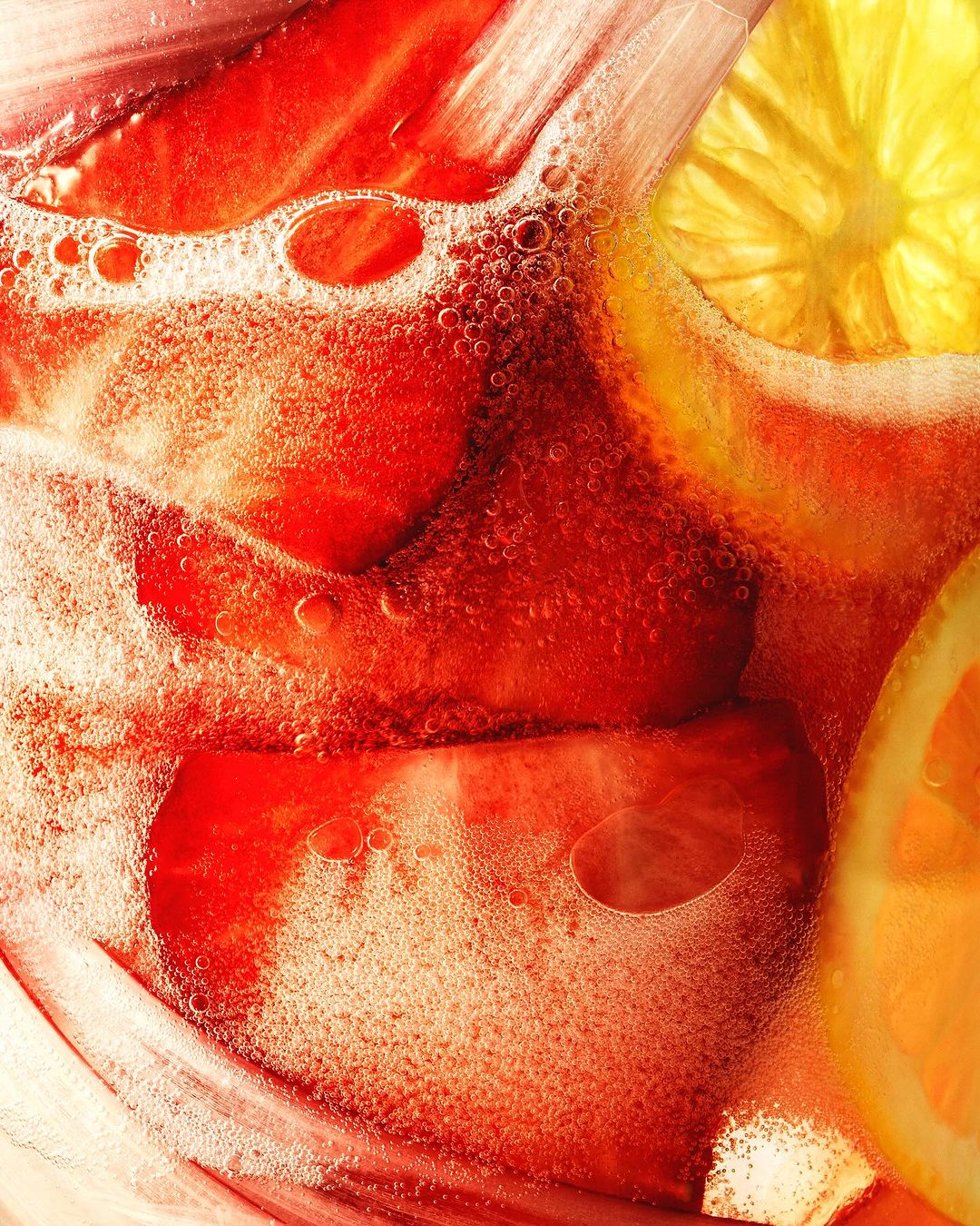 Close-up of a drink with sliced strawberries, lemons, and oranges with bubbles against a bright background.