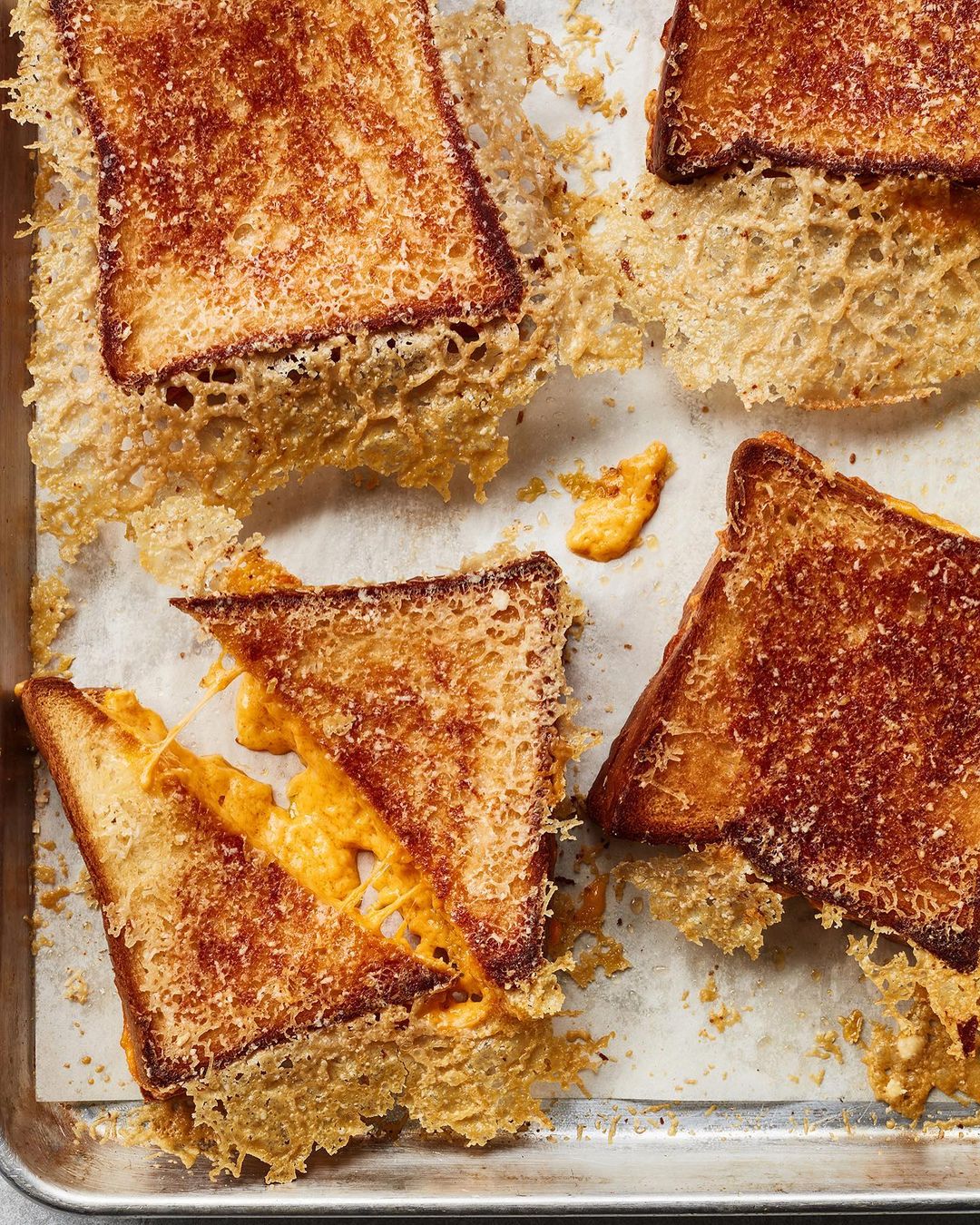 Overhead shot of multiple grilled cheese sandwiches with visible melted cheese on a baking sheet, creating a visually appealing culinary image.