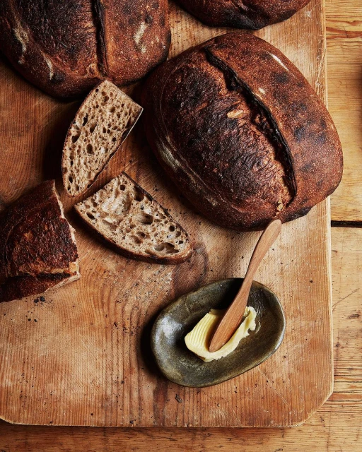 Artisan sourdough bread loaves on a rustic wooden cutting board, accompanied by butter and a small knife on a kitchen table.