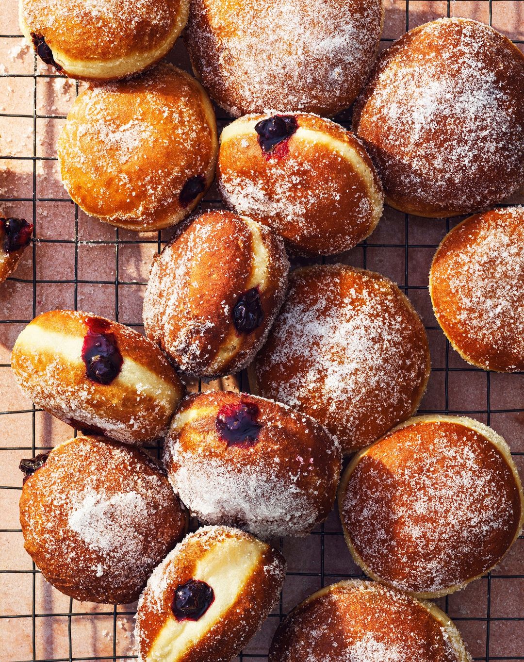 Overhead shot of several jelly doughnuts covered in powdered sugar, some split open to reveal purple filling. Perfect for dessert.