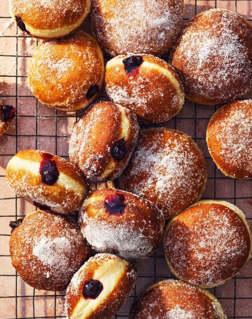Overhead shot of several jelly doughnuts covered in powdered sugar, some split open to reveal purple filling. Perfect for dessert.