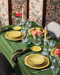 An elegantly set dining table draped in a green cloth with yellow patterned plates, crystal glassware, and pink candles.