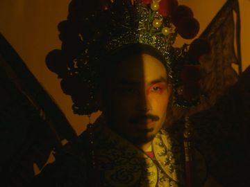 Portrait of a person wearing an ornate gold costume and headdress with half face in shadow against an orange background. Beauty shot.