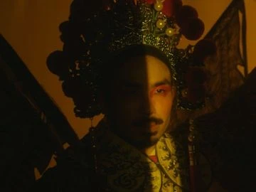 Portrait of a person wearing an ornate gold costume and headdress with half face in shadow against an orange background. Beauty shot.