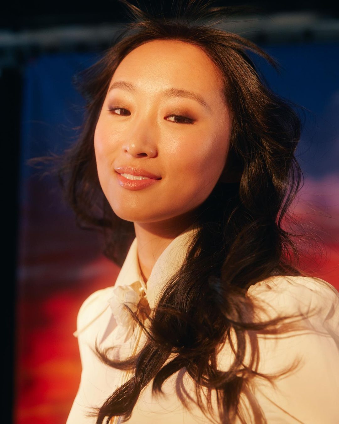 Portrait of an Asian woman with black hair wearing a light-colored shirt. She is looking directly at the camera in a studio environment.