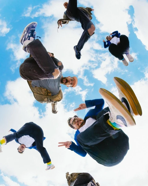 Group of diverse men in mid-air against a blue sky, low angle shot capturing dynamic poses and colorful casual fashion, creative composition.