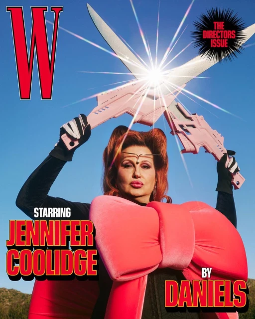 Jennifer Coolidge on magazine cover holding toy weapons in sunny outdoor setting. Red bow, blue sky, Hollywood celebrity, studio lighting.