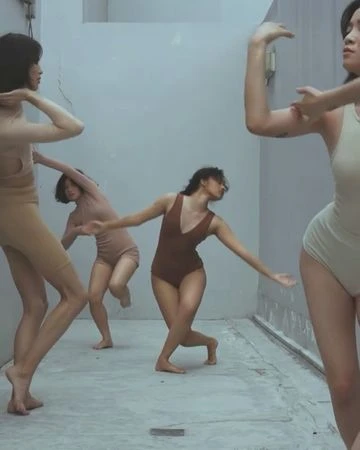 Five women in nude bodysuits strike expressive poses in a minimalist concrete interior, showcasing modern dance and movement.