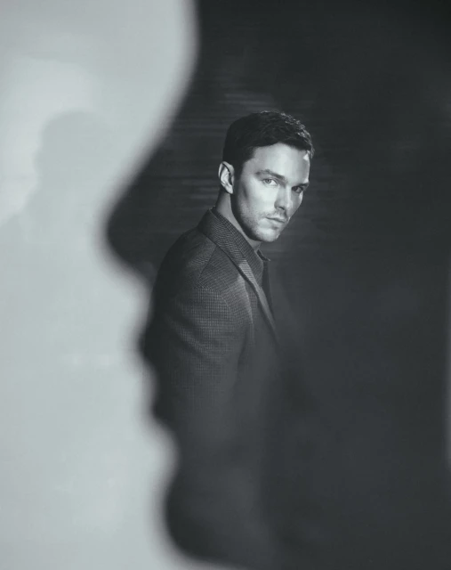 Black and white portrait of Nicholas Hoult wearing a suit jacket in a studio with light and shadow play for artistic effect.