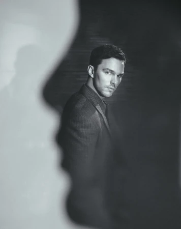 Black and white portrait of Nicholas Hoult wearing a suit jacket in a studio with light and shadow play for artistic effect.