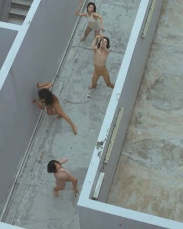 Overhead shot of four dancers in minimal clothing performing in a concrete architectural space with natural light, emphasizing movement and form.